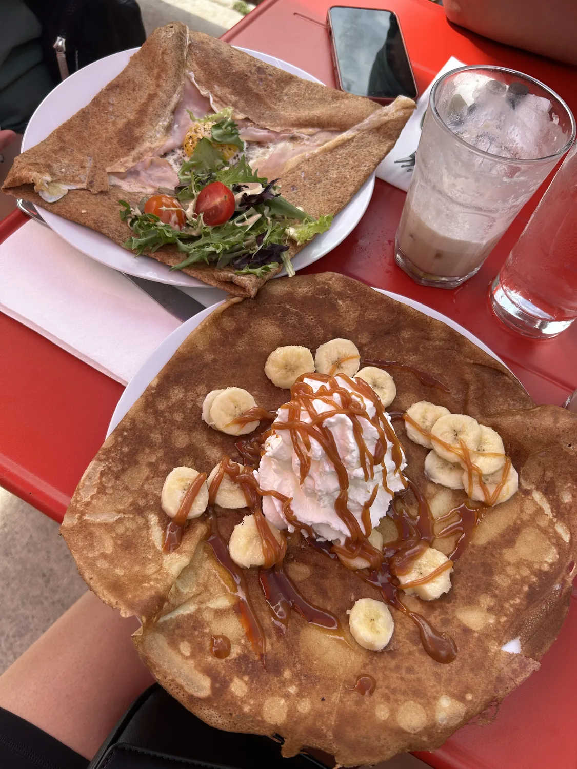 A savoury galette with ham and egg beside a banana-caramel sweet crêpe on the patio at Paris Crêpes Café